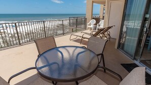 A balcony with a glass table and chairs, overlooking a beach with a fence and lounge chairs. - Phoenix V 307 1 Bedroom Condo (Orange Beach)