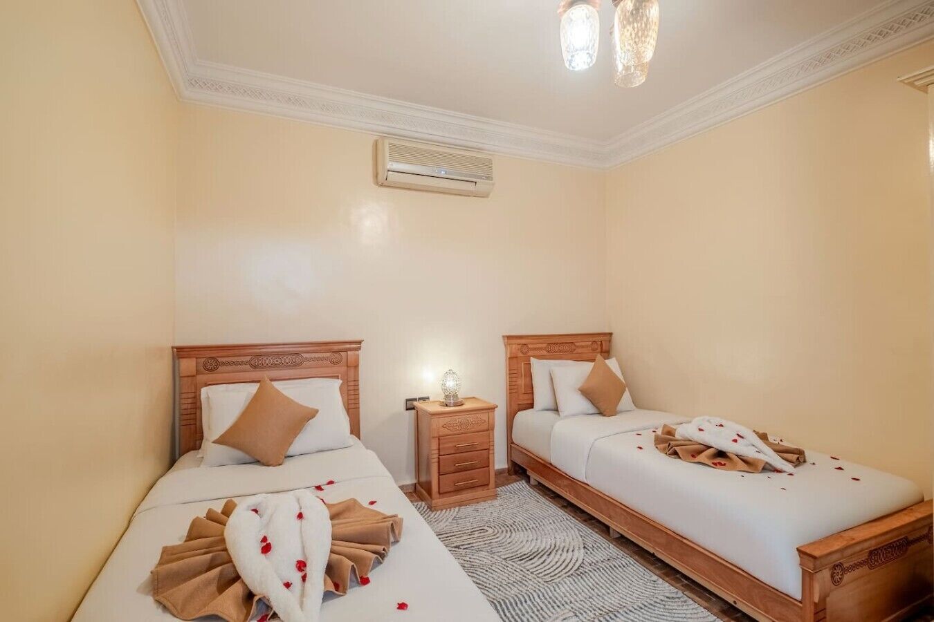 Una camera d'albergo con due letti, un comodino, una lampada e un lampadario.