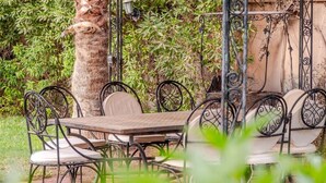 Un espace extérieur aménagé pour les repas, avec une table ronde et des chaises, le tout entouré de verdure.