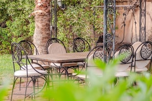An outdoor dining area with a round table and chairs, surrounded by greenery. - Villa Piscine / Hammam / 10 min de Centre (Marrakesh)