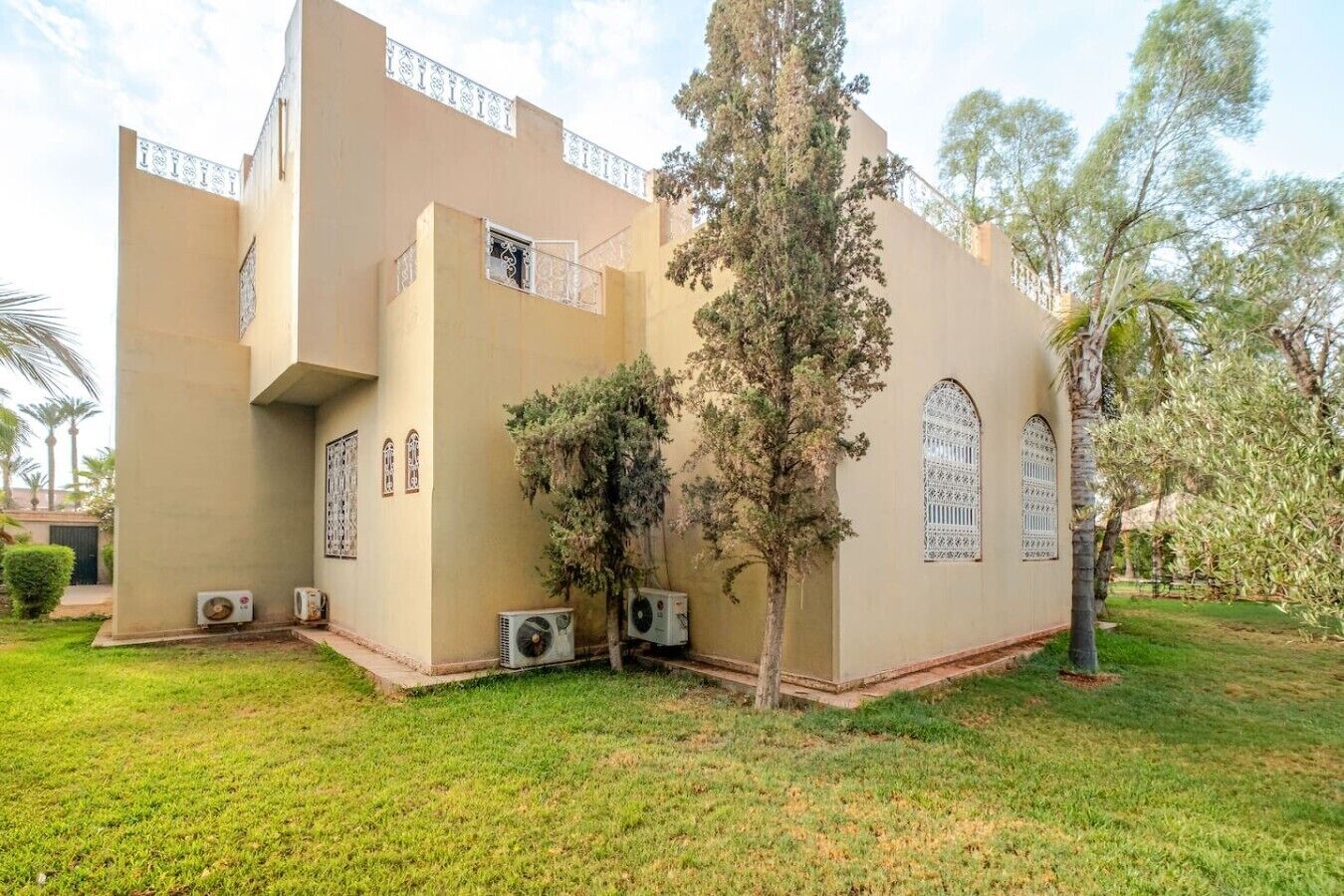 A building with a flat facade, multiple windows with decorative grills, and air conditioning units on the ground.