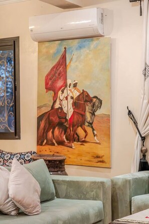 A living room with a painting of a historical scene, a sofa, and a decorative lamp. - Villa Piscine / Hammam / 10 min de Centre (Marrakesh)