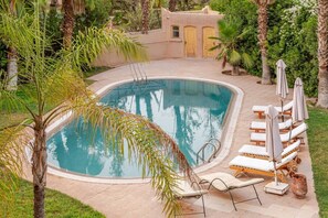 A swimming pool with lounge chairs and umbrellas, surrounded by palm trees and a building with doors. - Villa Piscine / Hammam / 10 min de Centre (Marrakesh)