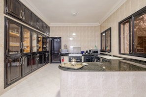 A modern kitchen with dark cabinetry, a central island, and a microwave. - Villa Piscine / Hammam / 10 min de Centre (Marrakesh)