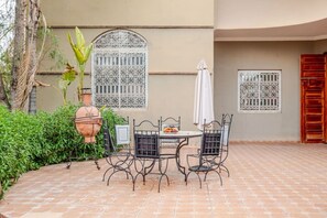 A patio with a round table and four chairs, a large terracotta pot, and a white umbrella. - Villa Piscine / Hammam / 10 min de Centre (Marrakesh)