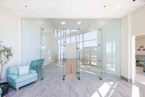 A modern office space with a glass partition, a teal sofa, and a potted plant. - Phoenix I 1114 1 Bedroom Condo (Orange Beach)