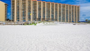 A high-rise hotel with multiple balconies, a sandy beach in the foreground, and a clear blue sky. - Phoenix V 911 1 Bedroom Condo (Orange Beach)