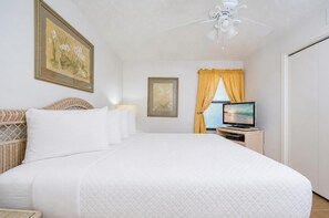 Une chambre d’hôtel avec un grand lit, une télévision, un ventilateur de plafond et des œuvres d’art accrochées aux murs.