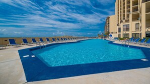 A large outdoor swimming pool with blue water, surrounded by lounge chairs and a tall building in the background. - Phoenix V 911 1 Bedroom Condo (Orange Beach)