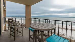 Ein Balkon mit Tisch und Stühlen, der Blick auf einen Strand mit einer Flagge hat.