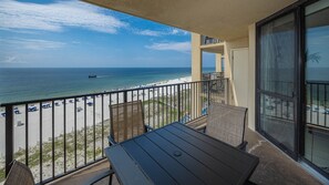 A balcony with a view of a beach and ocean, featuring a table and chairs. - Phoenix V 814 1 Bedroom Condo (Orange Beach)