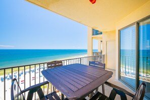 A balcony with a table and chairs, overlooking a beach with umbrellas and people. - Phoenix V 1211 1 Bedroom Condo (Orange Beach)