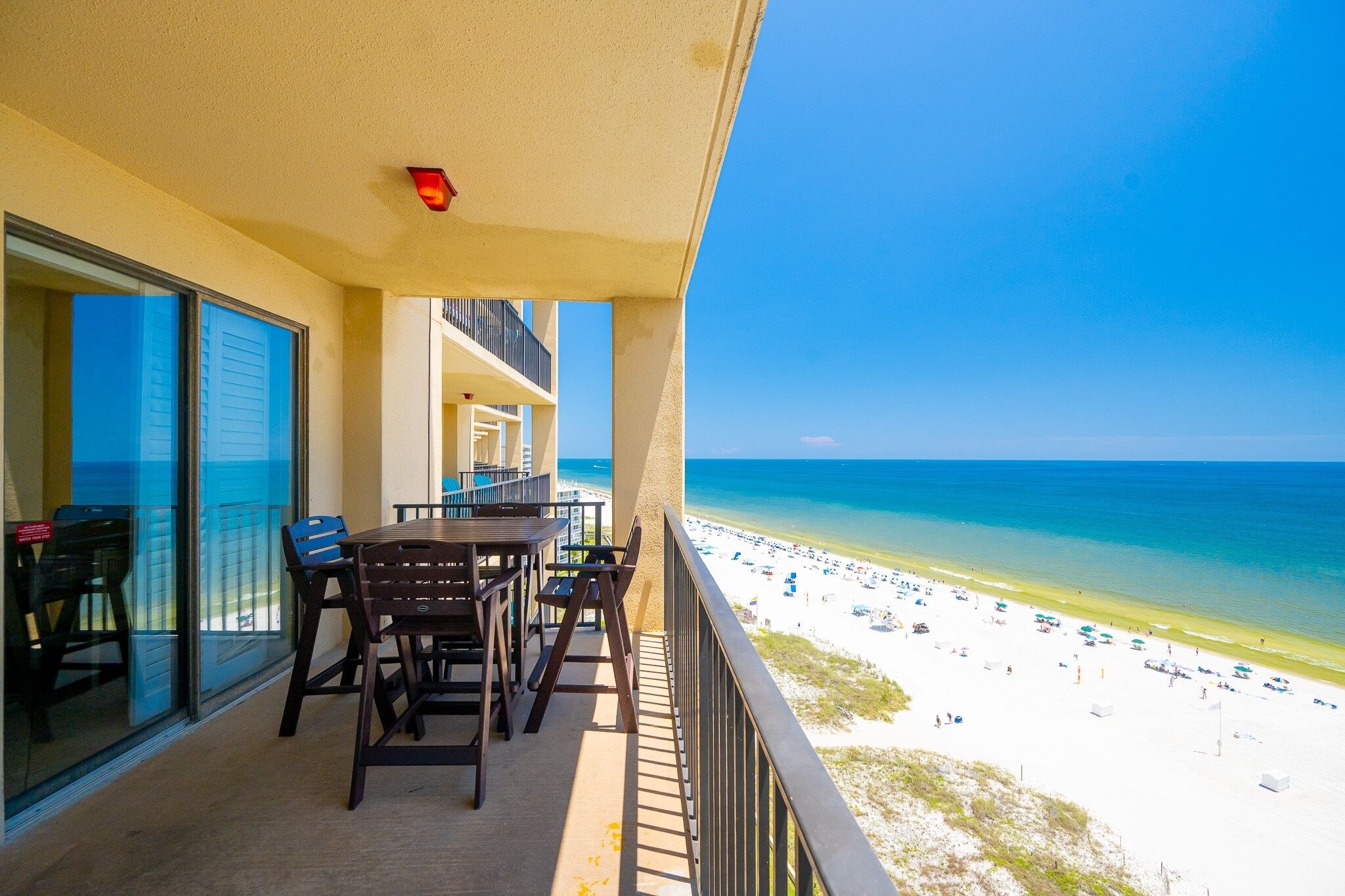 A balcony with a table and chairs, overlooking a beach with people and umbrellas.