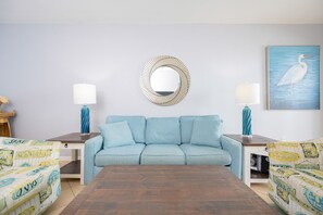 Un salon comprenant un canapé, deux tables d’appoint, une table basse, un miroir fixé au mur et un tableau encadré.