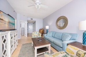 A living room with a television, a ceiling fan, a sofa, a coffee table, and a decorative mirror. - Phoenix V 1214 1 Bedroom Condo (Orange Beach)