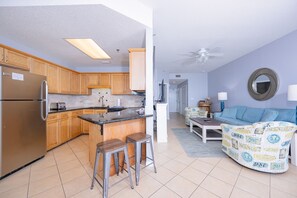 A modern kitchen with wooden cabinets, a stainless steel refrigerator, and a bar stool. - Phoenix V 1214 1 Bedroom Condo (Orange Beach)