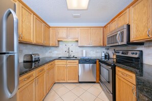 A modern kitchen with wooden cabinets, stainless steel appliances, and a tiled backsplash. - Phoenix V 1214 1 Bedroom Condo (Orange Beach)