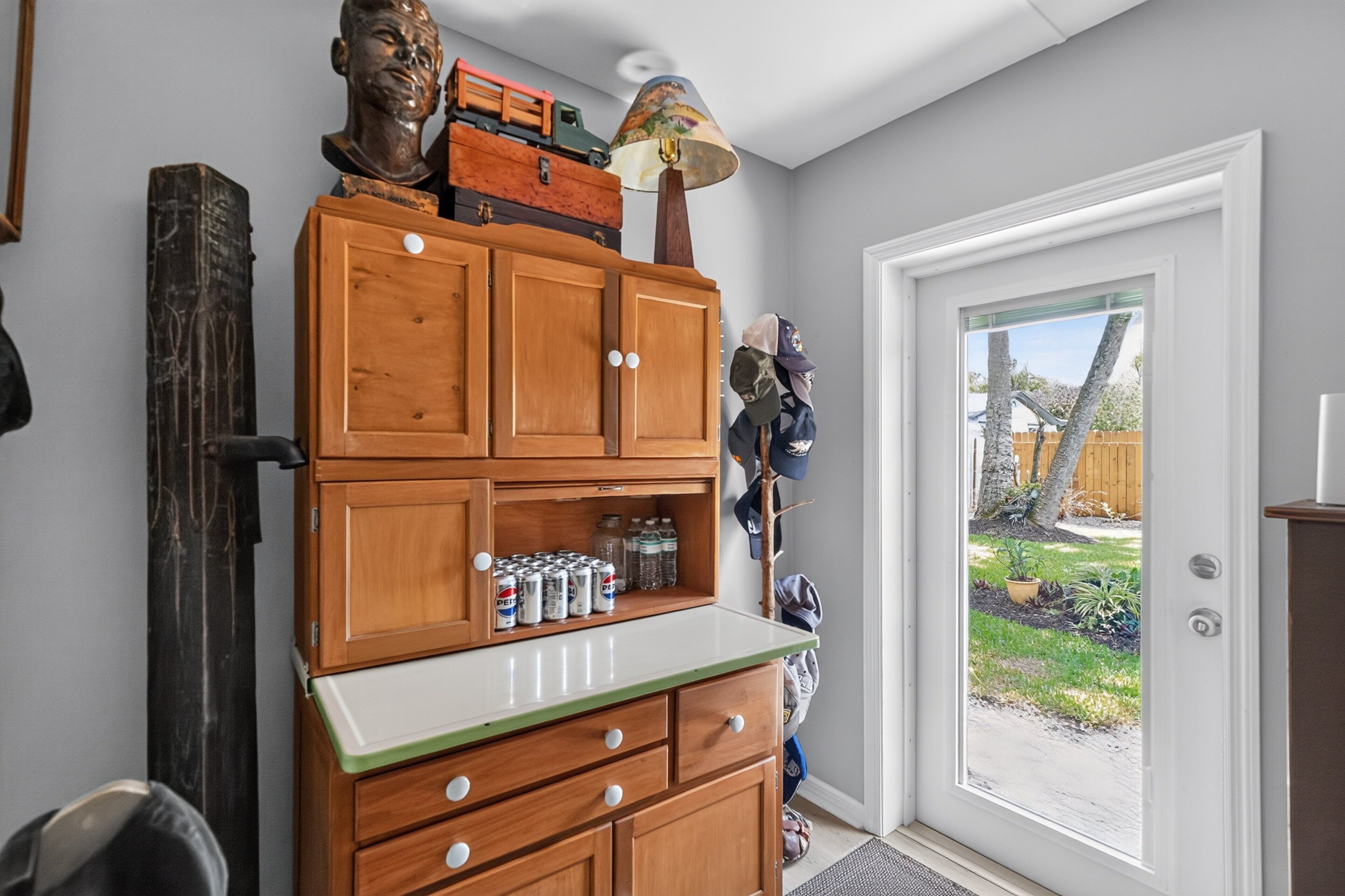 Un mueble de madera con cajones y un estante, una puerta con vista al exterior y una lámpara encima.