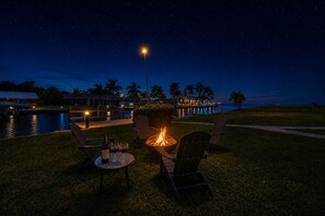 Ein Sitzbereich im Freien bei Nacht mit Feuerstelle, Stühlen und einem Tisch mit Getränken.