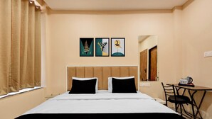 Una camera d'albergo con un letto, due cuscini neri, una testiera in legno, un tavolino con una sedia e tre opere d'arte incorniciate appese al muro.