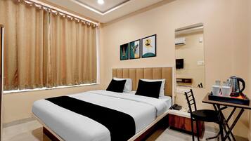 A hotel room with a bed, a chair, a table with a kettle, and a mirror.