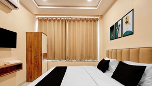Una camera d'albergo con un letto, un armadio in legno, una TV a schermo piatto, una finestra con tende e opere d'arte appese al muro.