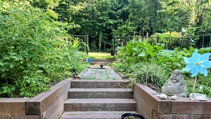Een houten trap die leidt naar een tuin met een vogelhuisje, een beeld en een bloempot.