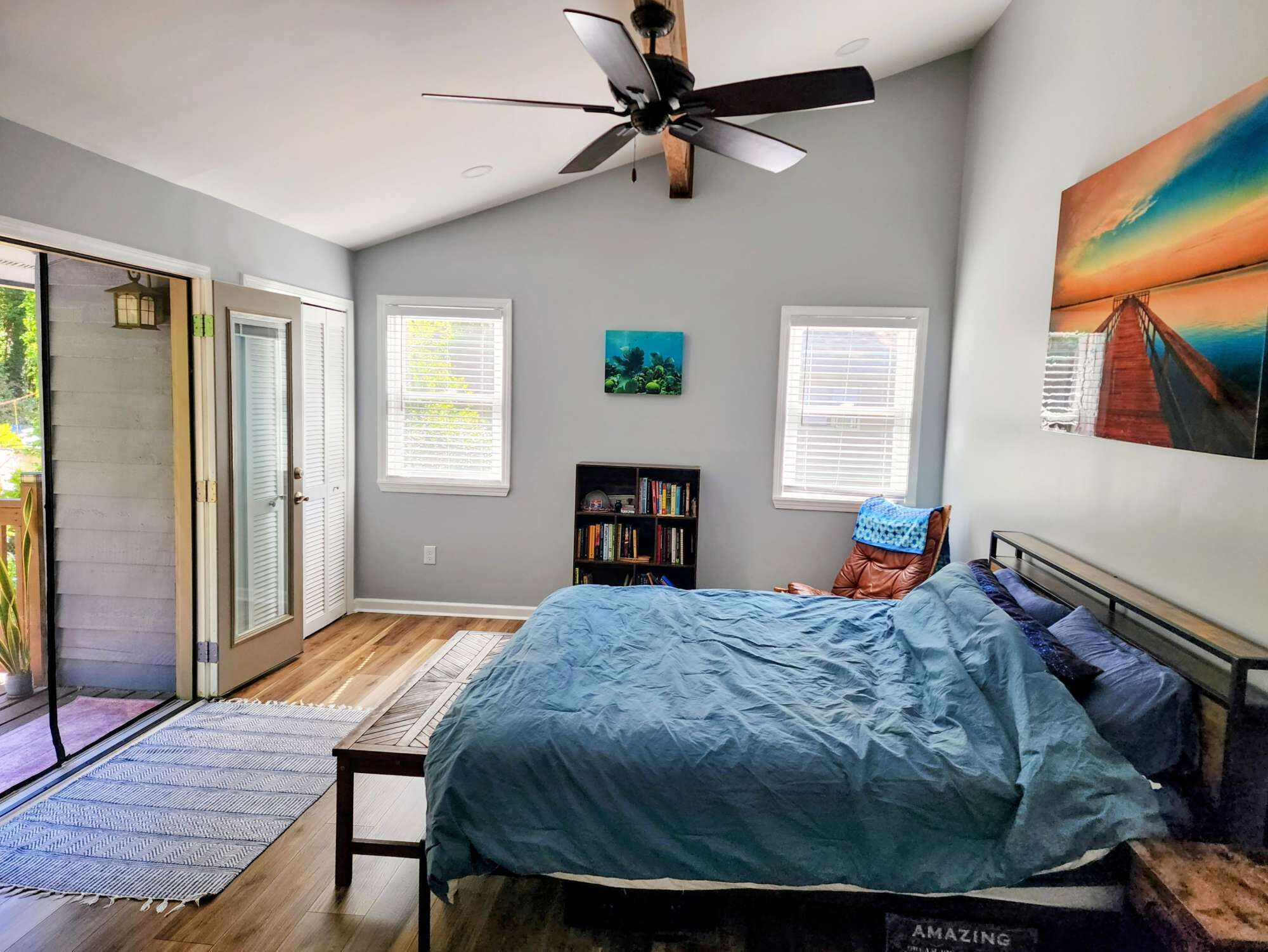 A bedroom with a bed, a ceiling fan, a bookshelf, and a painting on the wall.