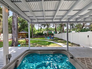 Un espace extérieur abrité avec un jacuzzi, une terrasse en bois, une cour clôturée et un gazebo en arrière-plan.