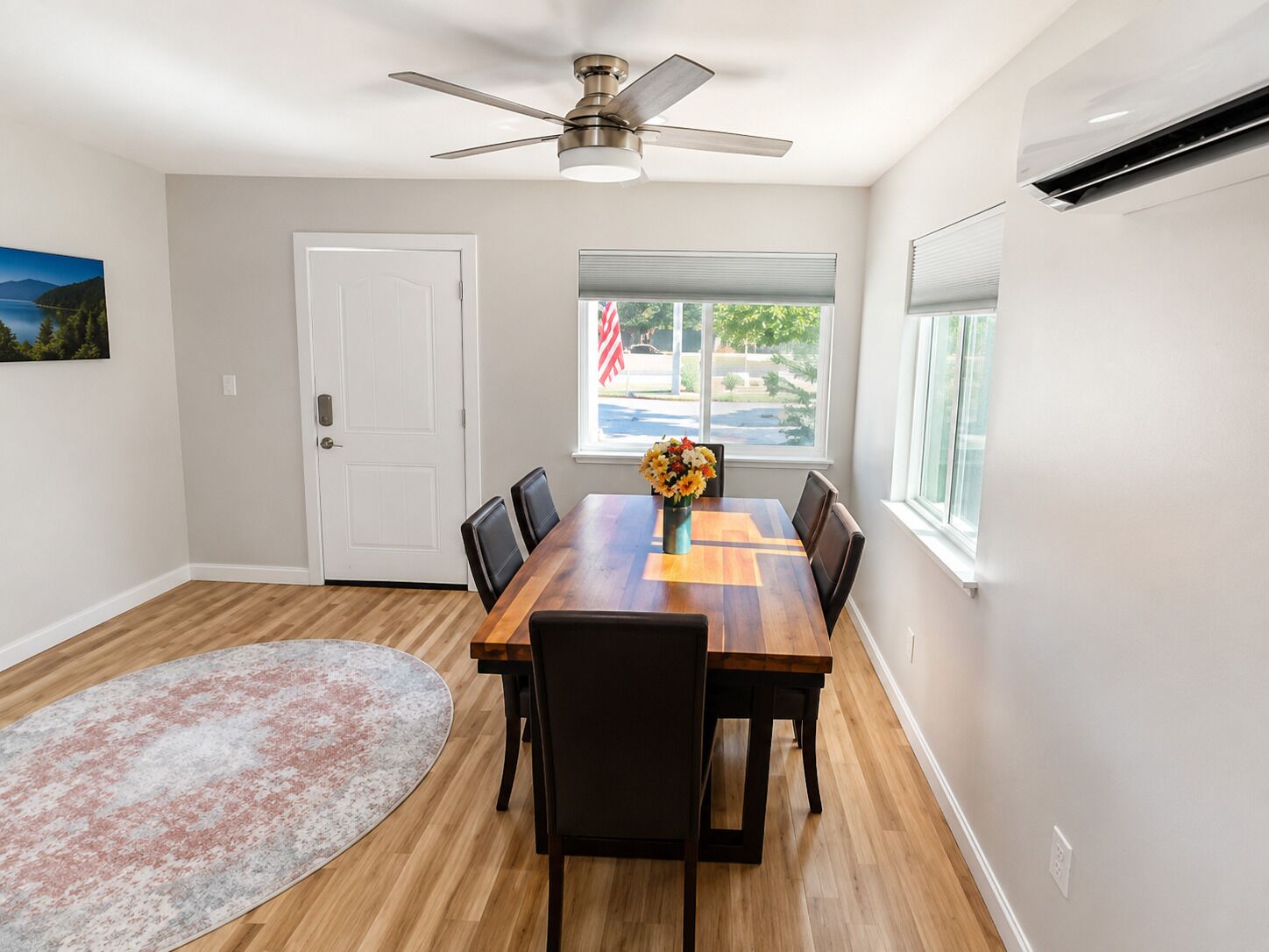 A dining area with a wooden table, chairs, a ceiling fan, a window with blinds, and a rug.