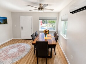 Un coin repas avec une table en bois, des chaises, un ventilateur de plafond, une fenêtre avec des stores et un tapis.