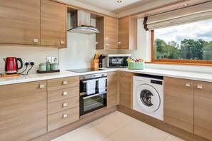 Una cocina moderna con armarios de madera, microondas, hervidor y lavadora.