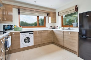 Een moderne keuken met houten kastjes, een ingebouwde wasmachine, een magnetron en een koelkast.