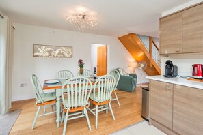 Een eetruimte met een tafel gedekt voor vier personen, een kroonluchter, en een keuken met moderne apparatuur.