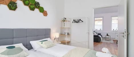 Ein modernes Hotelzimmer mit einem Bett, einem Nachttisch, einem Spiegel und Blick in das angrenzende Zimmer.