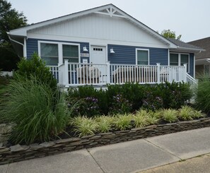 A single-story house with a front porch, a stone retaining wall, and a variety of plants. - Downtown Rehoboth Beach Cozy Beach Getaway! (Rehoboth Beach)