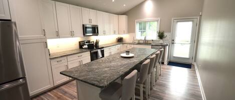 Una cocina moderna con armarios blancos, un refrigerador de acero inoxidable, un microondas y una isla alargada con taburetes de bar.