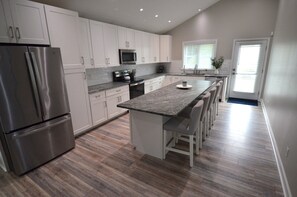 A modern kitchen with white cabinetry, stainless steel appliances, a central island with bar stools, and a microwave above the stove. - Downtown Rehoboth Beach Cozy Beach Getaway! (Rehoboth Beach)