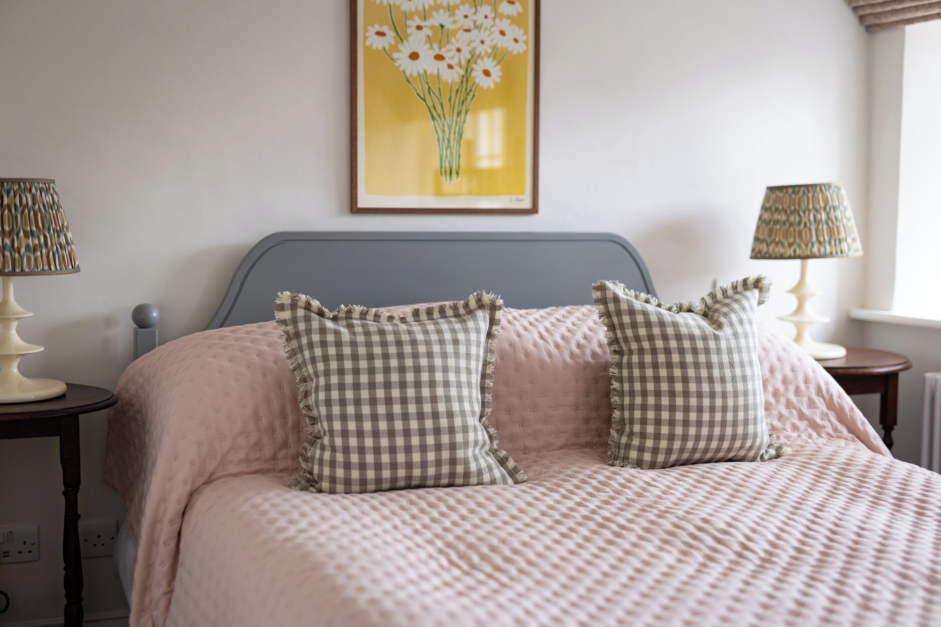 A bedroom with a bed, two bedside lamps, a wall-mounted picture, and a window.