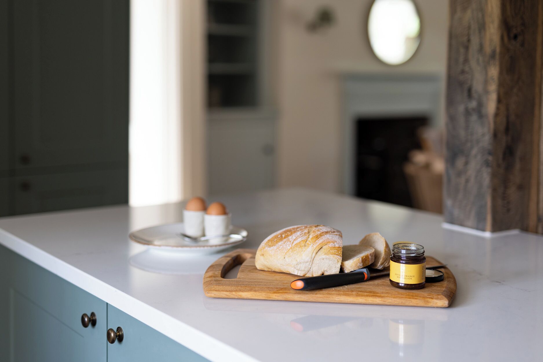 A kitchen counter with a loaf of bread, a jar of jam, and two eggs on a plate.