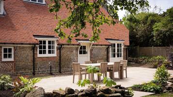 A brick house with a tiled roof, a stone wall, and a garden with a patio table and chairs.