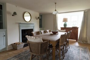 A dining room with a wooden table, wicker chairs, a fireplace, and a large mirror on the wall.