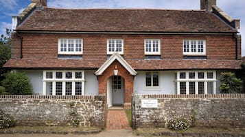 A traditional brick house with a symmetrical facade, a central entrance with a decorative arch, and a stone wall with a sign indicating the property name.