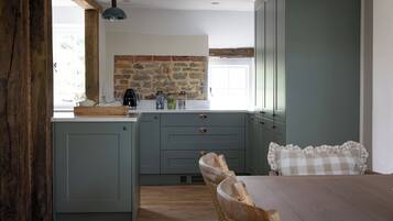 Una cocina con pared de piedra, vigas de madera y un comedor con mantel a cuadros.