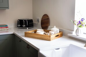 A kitchen counter with a wooden tray holding white cups and a teapot, a vintage radio, and a wooden bowl.