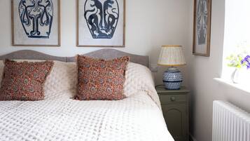 Un dormitorio con una cama, dos almohadas, una mesita de noche, una lámpara y decoración en la pared.