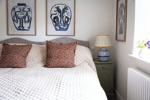 Een slaapkamer met een bed, twee kussens, een nachtkastje, een lamp en decoratie aan de muur.