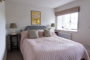 A bedroom with a bed, two bedside lamps, a radiator, a window with a valance, and a framed picture on the wall.