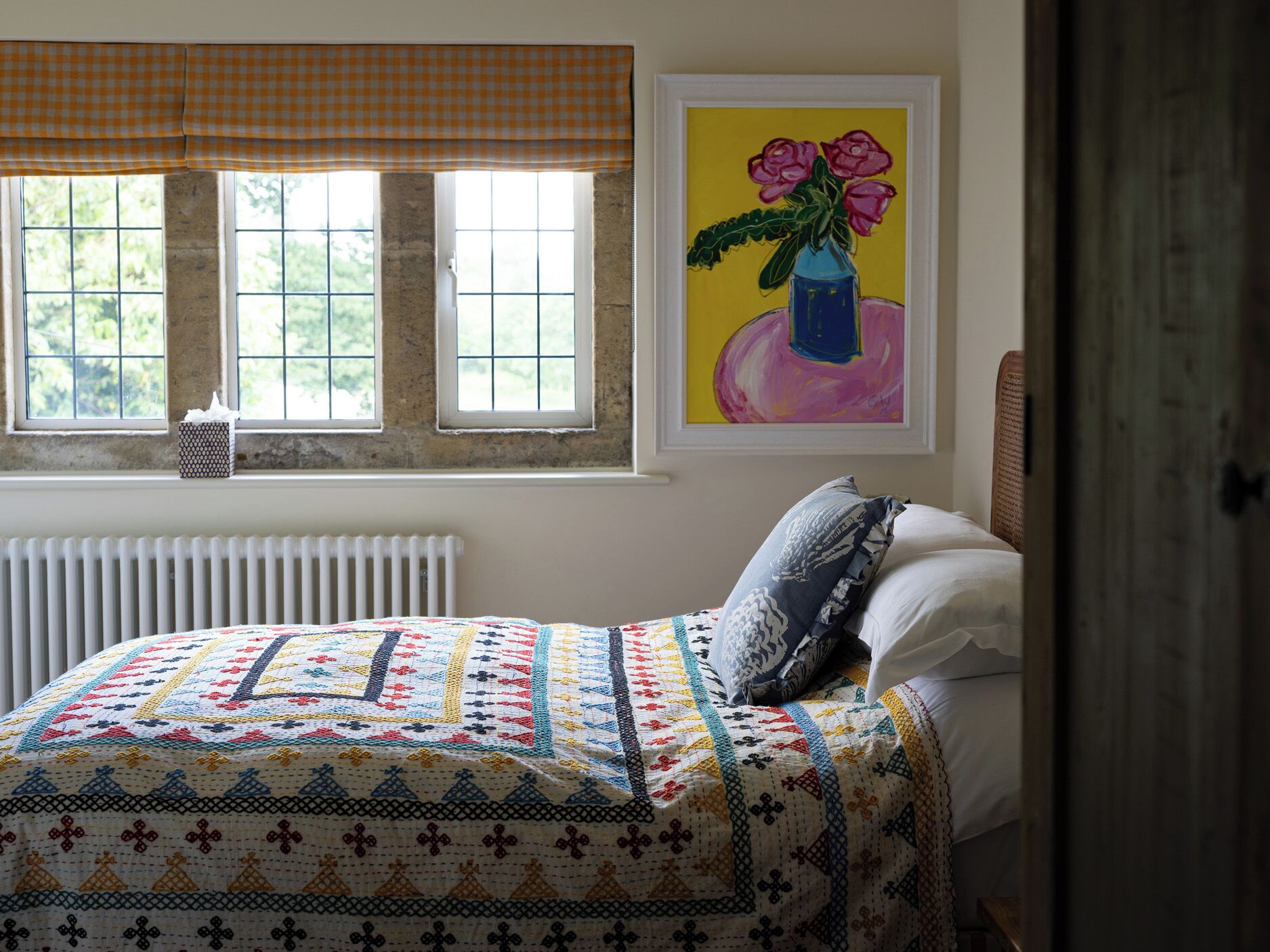 A bedroom with a bed, a radiator, a window with a checkered blind, and a painting on the wall.