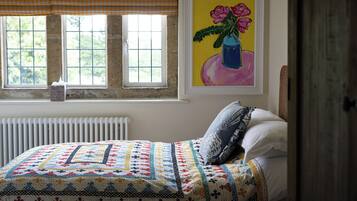 A bedroom with a bed, a radiator, a window with a checkered blind, and a painting on the wall.